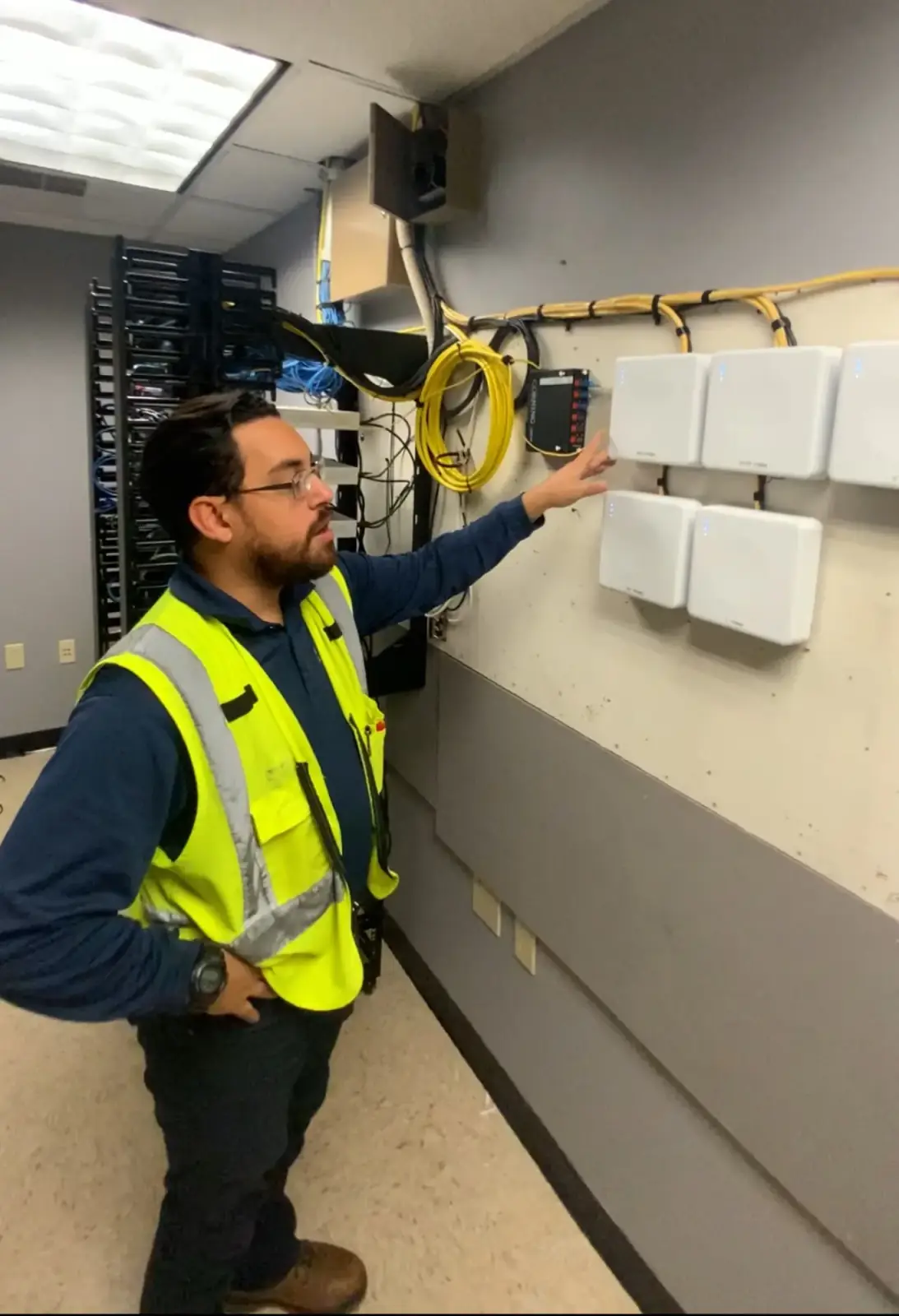 DIST technician in a hi-vis vest mounting wireless access points beside a network rack
