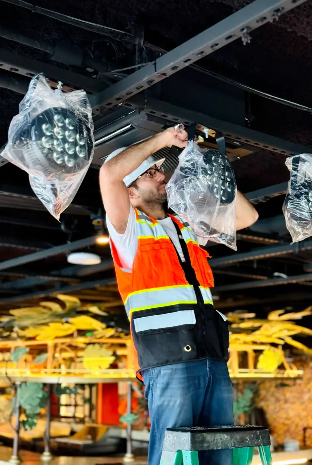 DIST installer in a hi-vis vest rigging fixtures in a venue ceiling