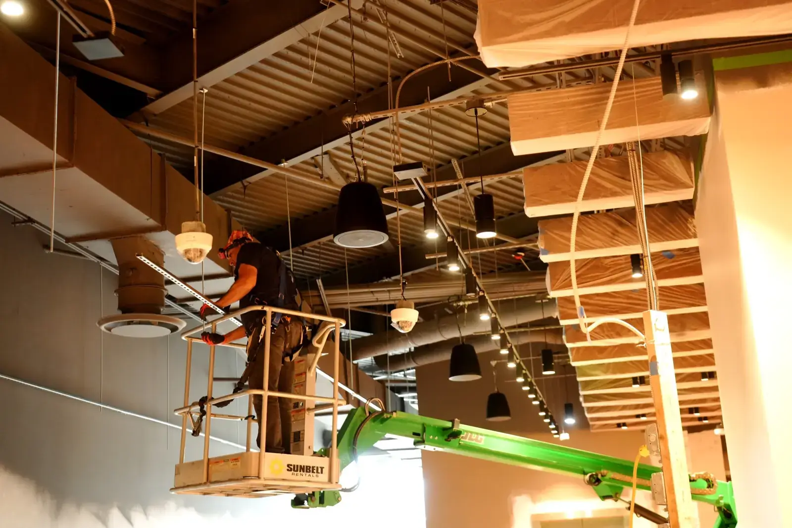 DIST technician on a lift installing dome cameras and pendant speakers in a restaurant ceiling