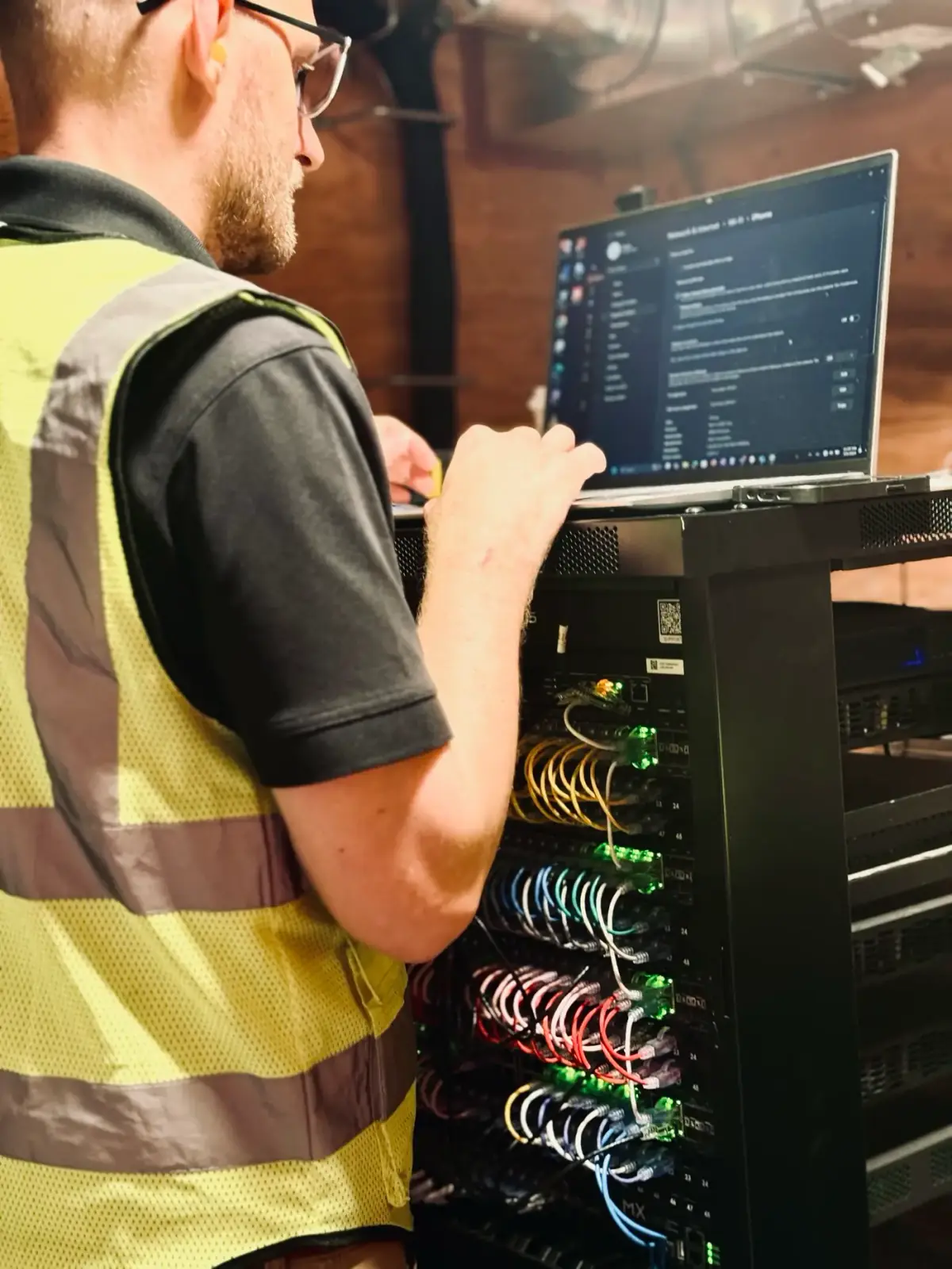 DIST technician in a hi-vis vest testing network connections at an equipment rack